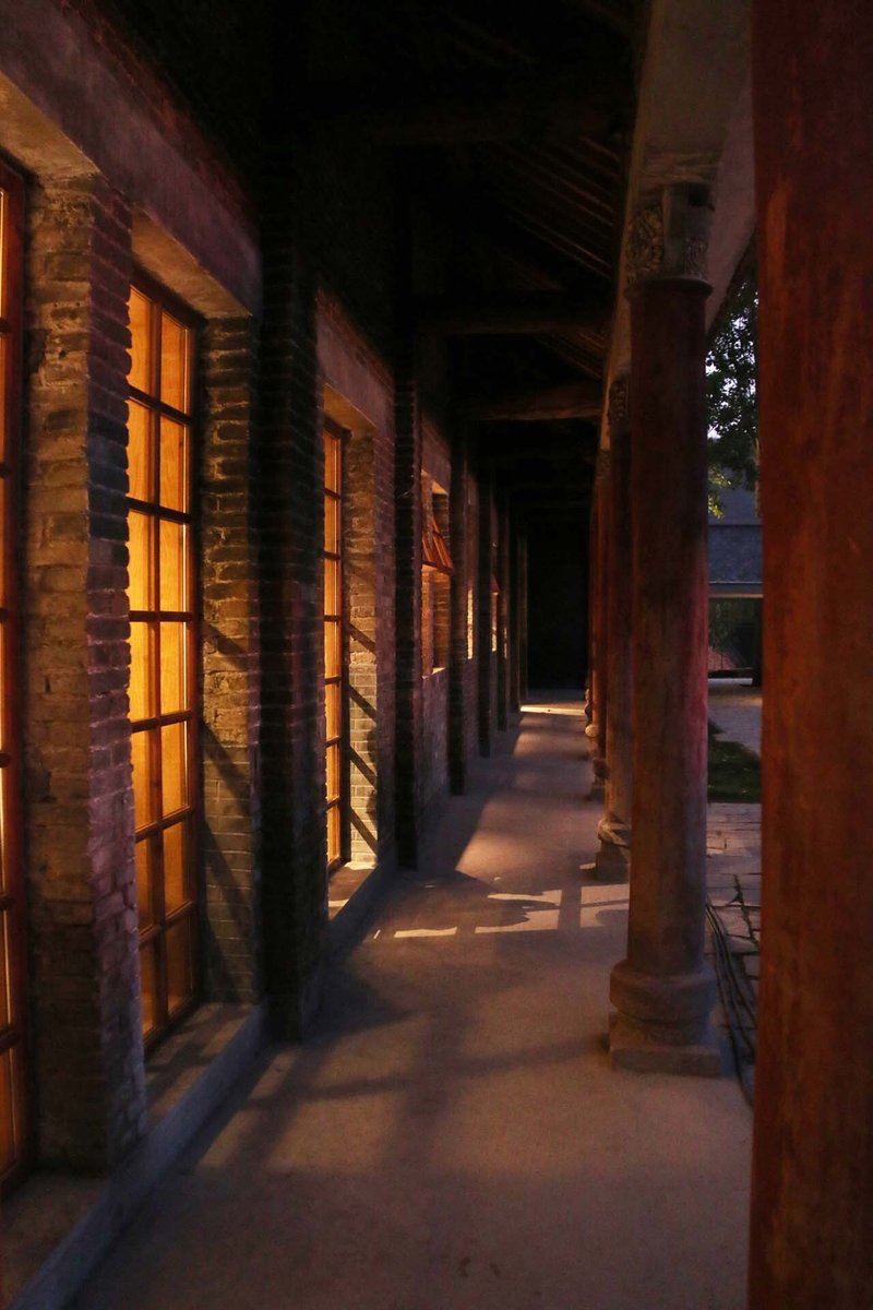 Covered exterior corridor with exposed brick columns and timber roof beams at dusk