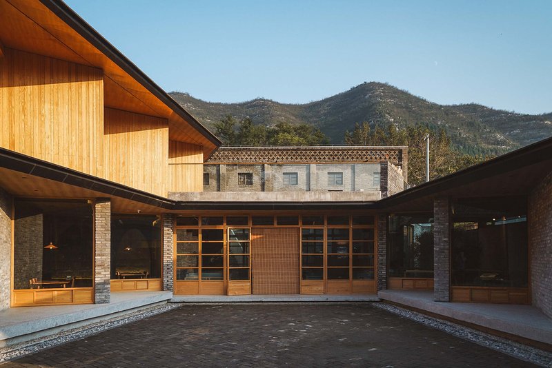 Courtyard view of timber-clad volumes with sloped roofs and stone base against distant mountains