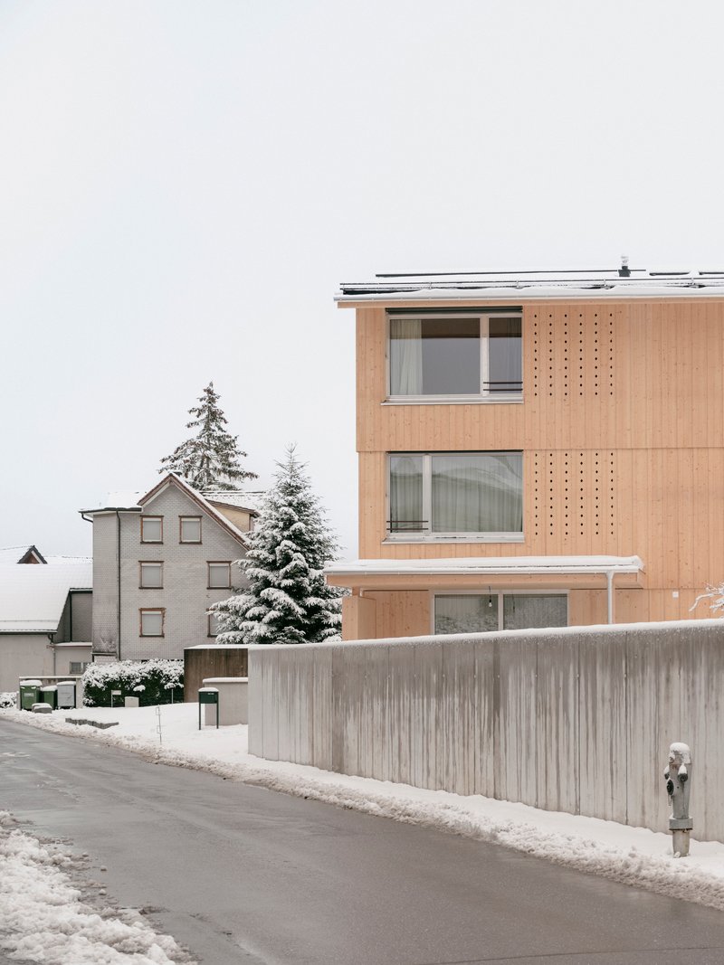 Timber facade with perforated screens beside horizontal windows backed by a weathered concrete boundary wall