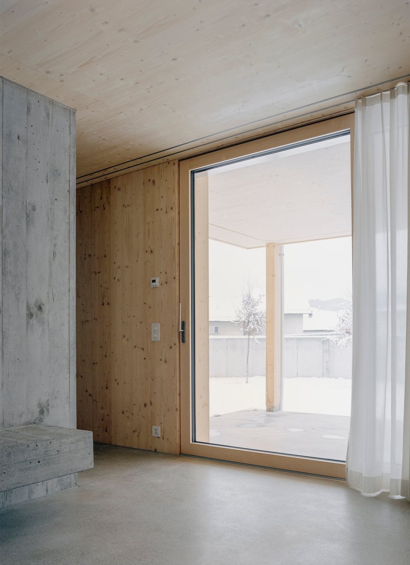 Interior room with plywood ceiling and concrete walls framing a glazed door to a snow-dusted terrace