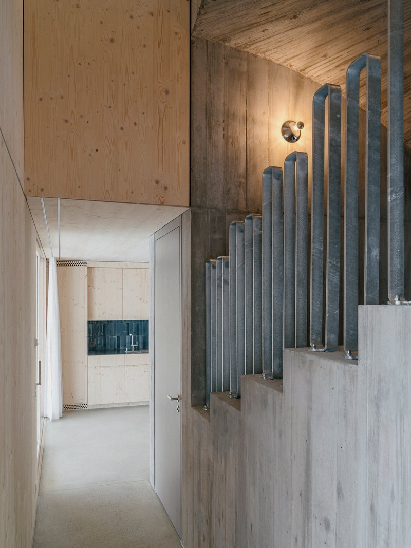 Concrete staircase with vertical metal pipe balustrade ascending through a double-height corridor