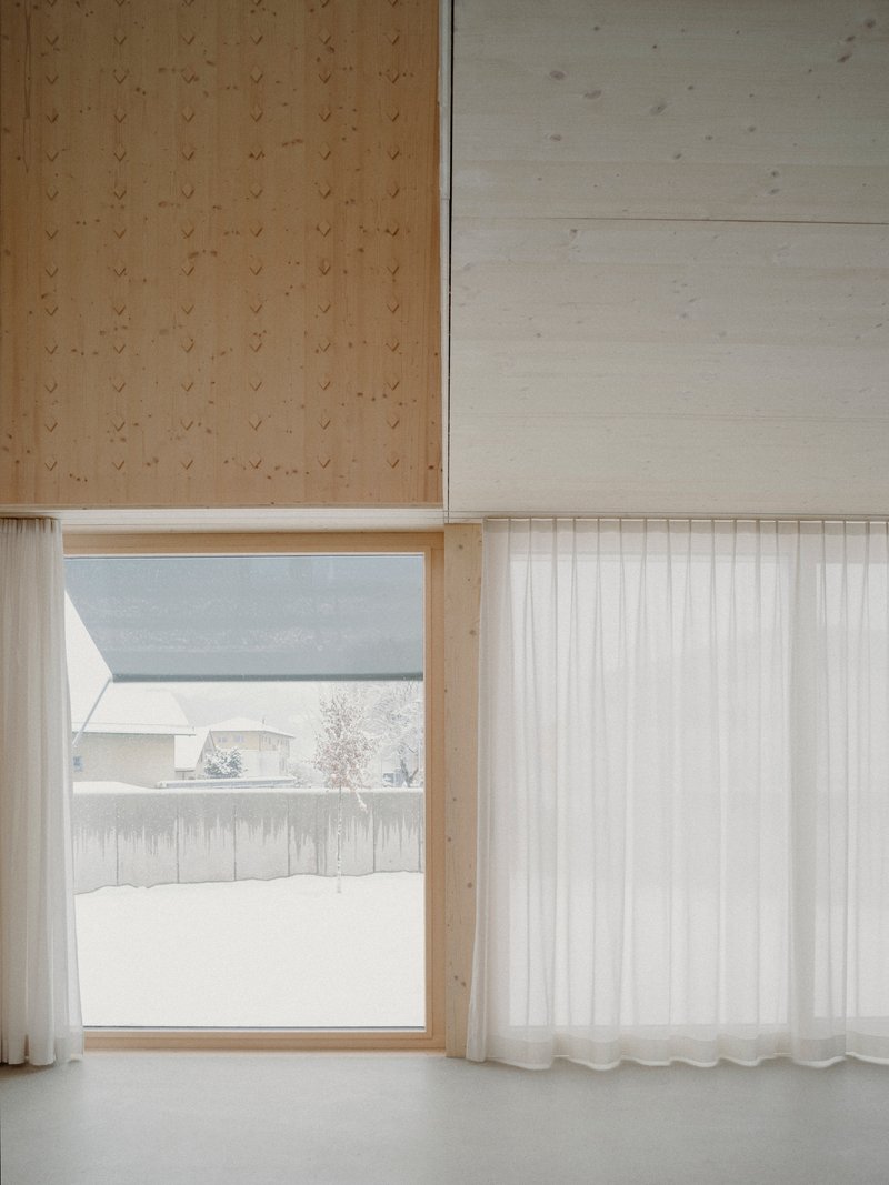 Window opening framing snowy landscape beyond a sheer curtain and plywood paneled walls