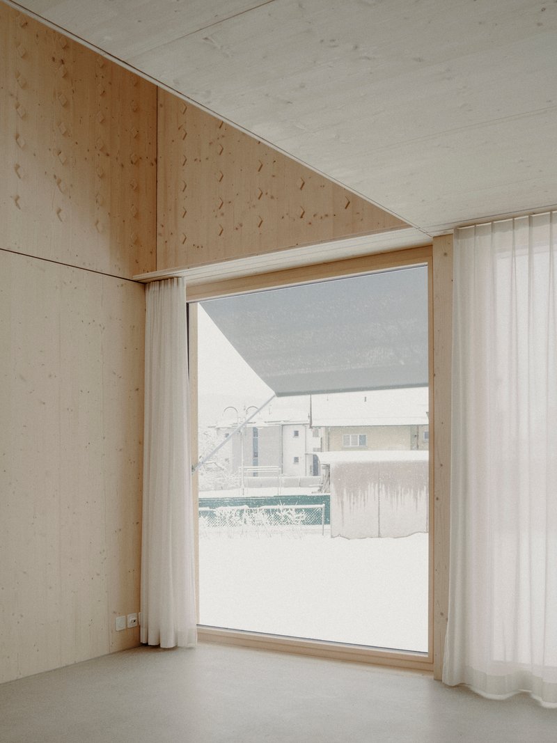Light plywood interior corner with floor-to-ceiling window framing a snowy courtyard view