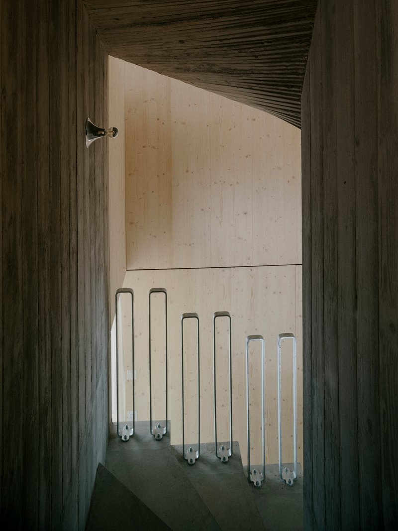 Timber-framed doorway revealing concrete staircase with rows of translucent tube lights along the wall