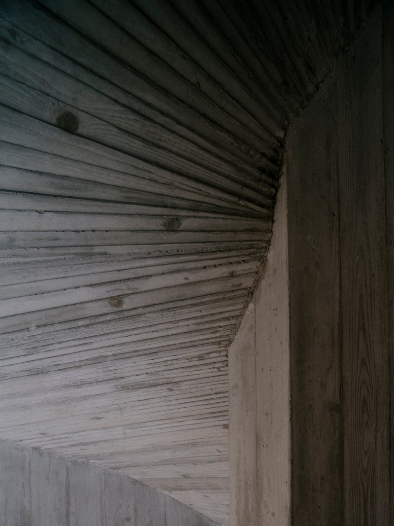 Close-up of ribbed timber ceiling meeting a board-formed concrete wall at the corner