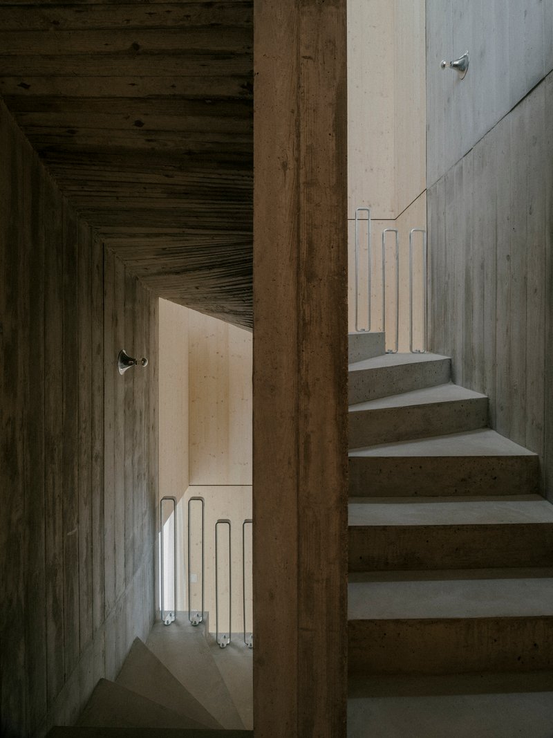 View through timber doorway showing concrete stairs ascending alongside a corridor with tube lighting below