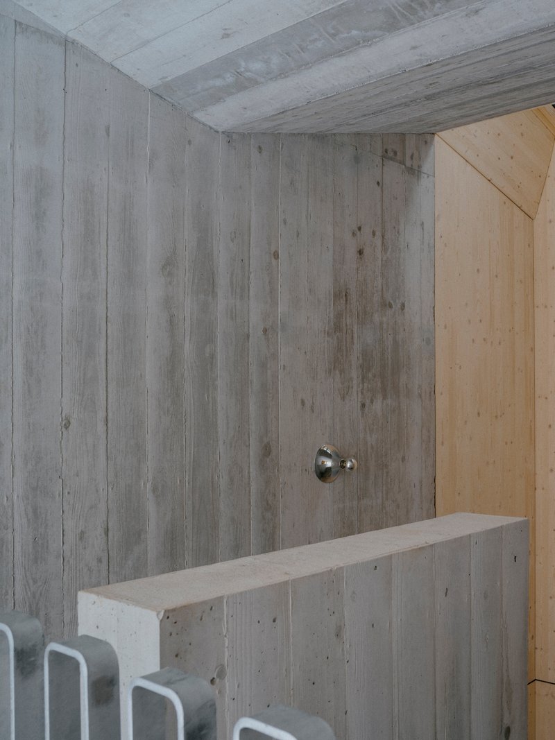 Board-formed concrete wall with a single sconce above a low concrete bench