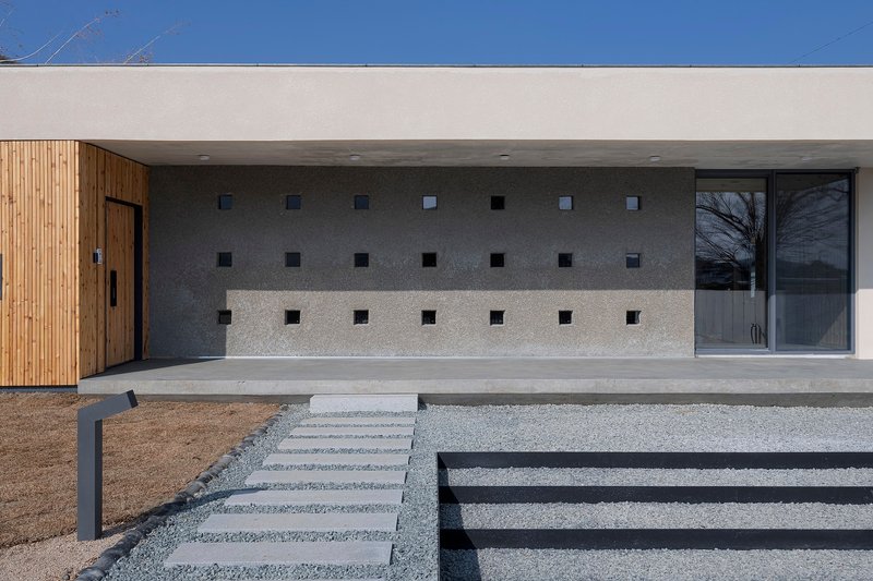 Facade with grid of square openings in concrete wall flanked by timber cladding and glazing