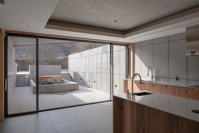 Kitchen with timber cabinetry and concrete walls opening to courtyard through sliding glass doors