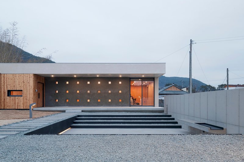 Entry facade with perforated concrete wall and wide stairs at dusk under overcast sky