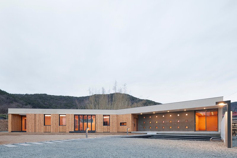 Horizontal timber-clad facade with scattered punched windows and illuminated concrete porch at dusk