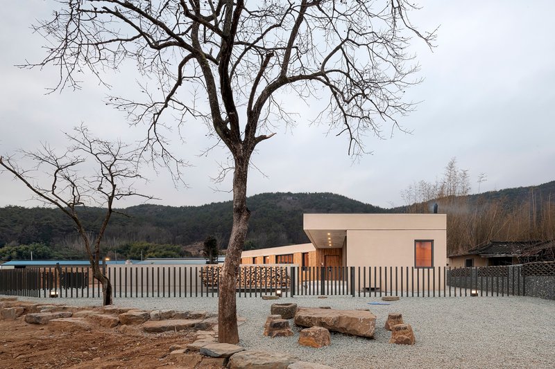 White concrete house behind vertical slatted fence with bare winter tree and hillside backdrop