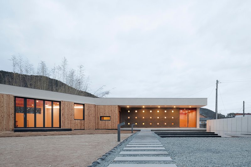 Horizontal facade combining timber cladding and white concrete with recessed square openings at dusk