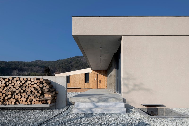 Entry steps leading to recessed entrance with stacked firewood wall and distant timber building