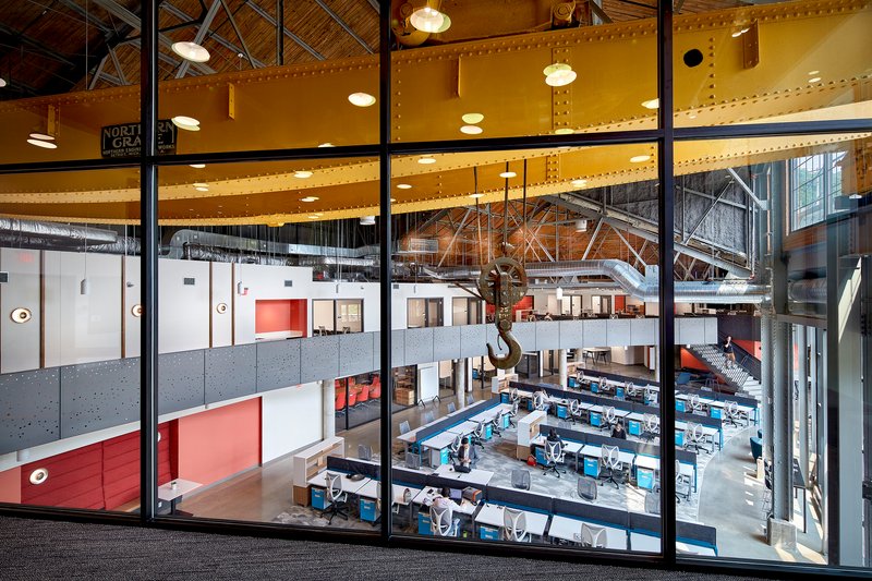 View through glazed partition wall overlooking the open workspace and yellow-painted crane beam at upper level