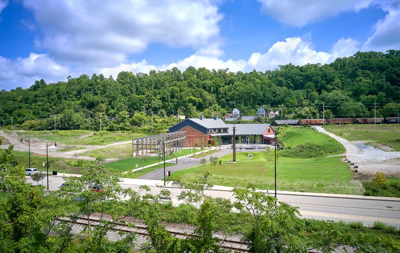Wide view of the campus set in a green valley with young trees lining the access road and wooded hillside beyond