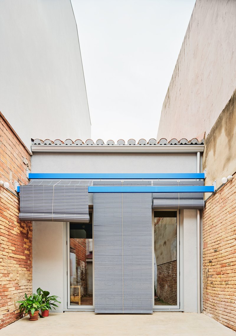 Courtyard framed by brick walls with corrugated metal shutters and blue painted steel lintel under overcast sky
