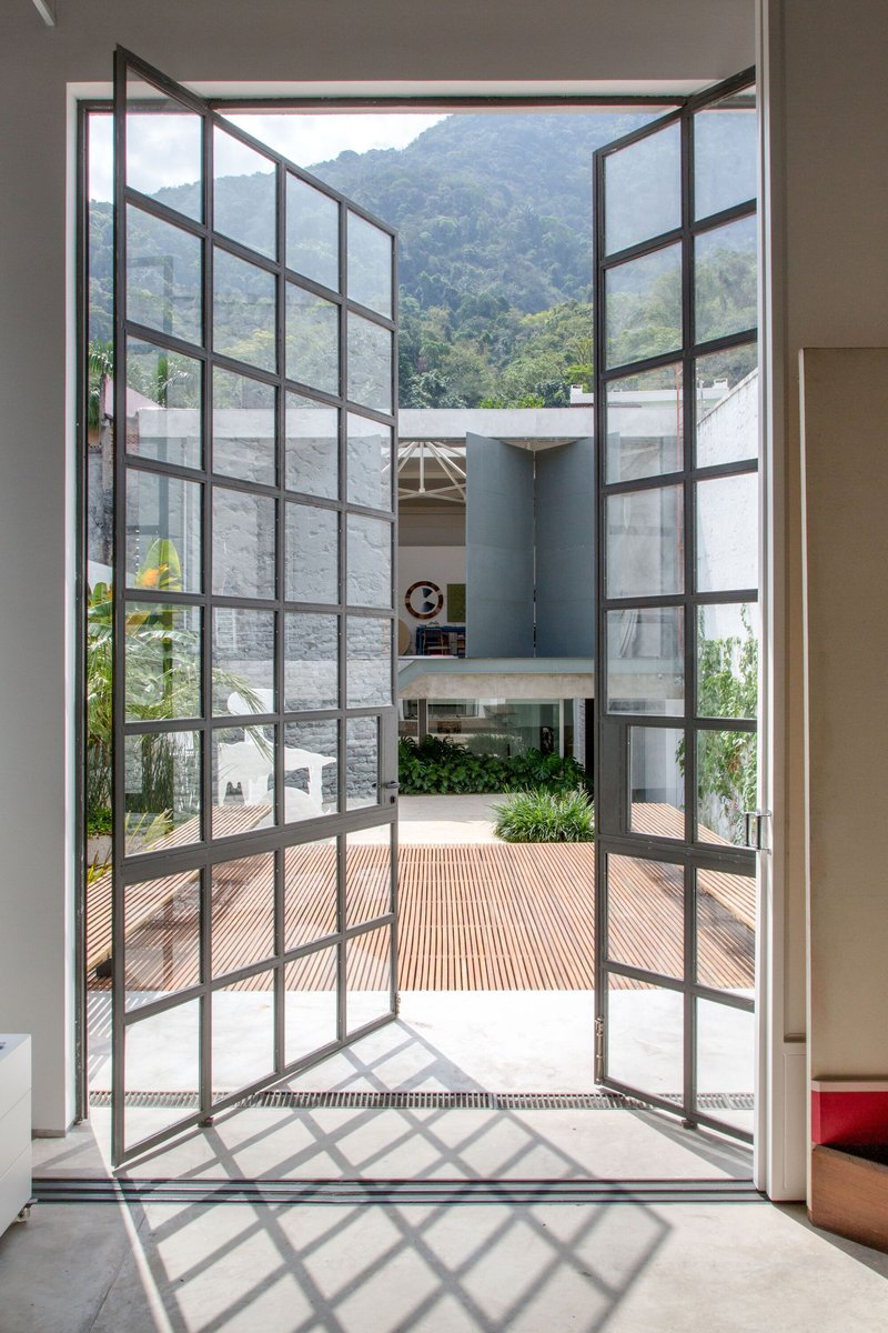 Open steel-framed glass doors leading to a timber deck courtyard with mountains visible beyond