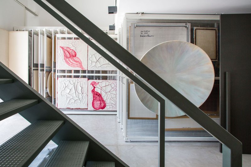 Steel staircase framing a view through wire mesh screens to a balcony with pink fabric artwork