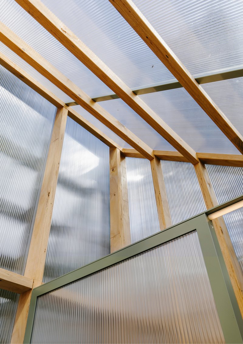 Sloped ceiling with exposed timber rafters and translucent corrugated polycarbonate panels under clouds