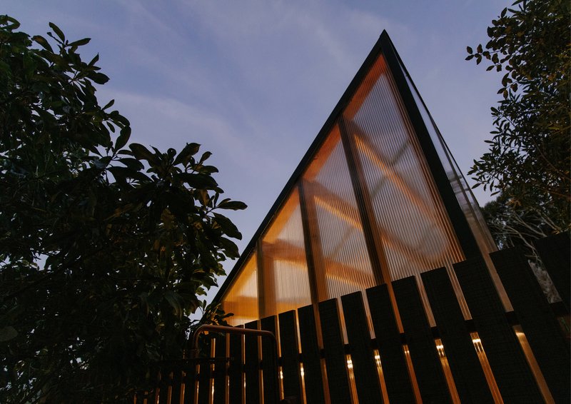 Triangular gable end with translucent polycarbonate cladding and exposed timber structure illuminated at twilight