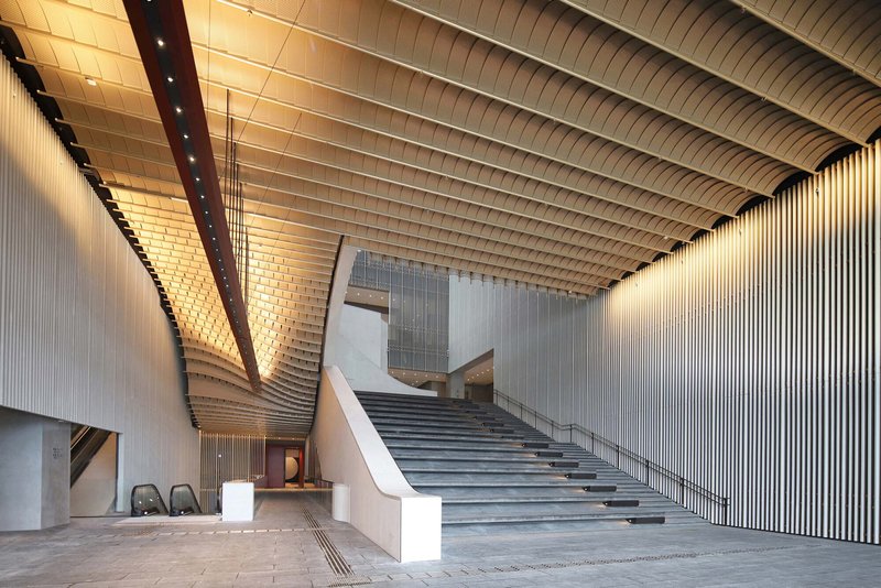 Interior lobby with curved horizontal ceiling panels and a wide staircase ascending to upper levels