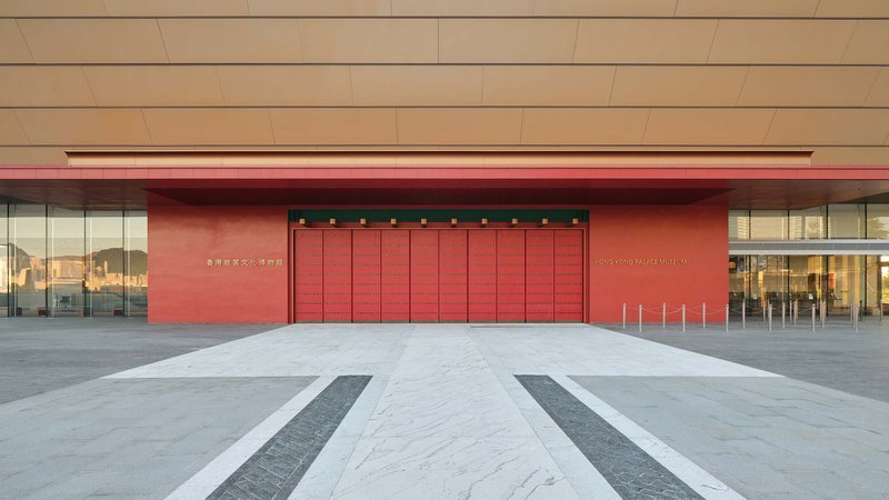 Entrance plaza with red folding doors and striped paving beneath a beige canopy
