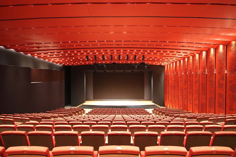 Auditorium interior with textured red acoustic ceiling panels and matching upholstered seating facing the stage