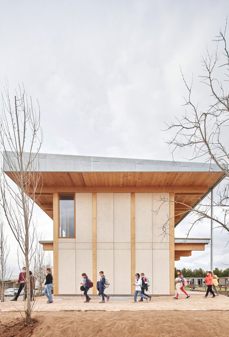 Entrance pavilion with exposed timber soffit sheltering schoolchildren walking across sandy ground