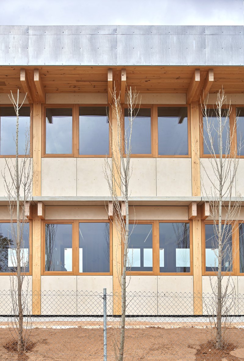 Two-story timber facade with horizontal banding and bare winter trees behind chain-link fence