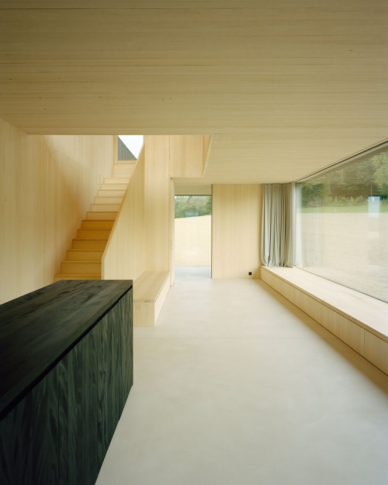 Light-filled living space with pale timber walls, concrete floor and a window seat facing garden views