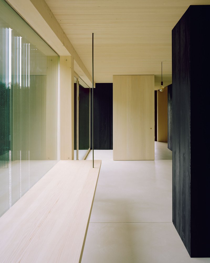 Corridor with dark timber wall panels and full-height glazing reflecting the interior circulation