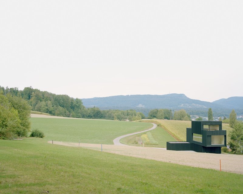 Distant view of the rectilinear volumes positioned beside a winding road through rolling green hills