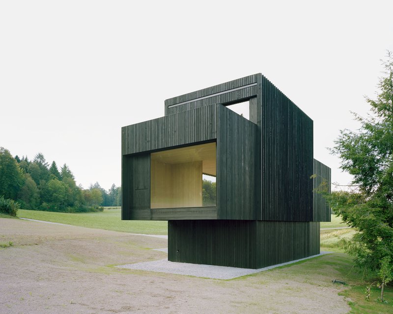Corner elevation showing vertical timber cladding with deep recessed openings revealing interior volumes