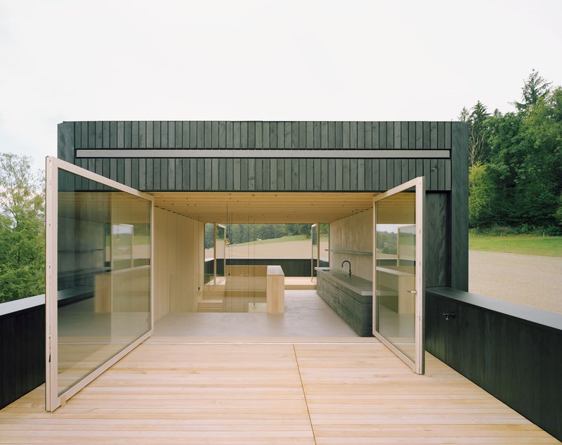 Open glazed threshold with pivoting glass doors connecting light wood interior to timber deck