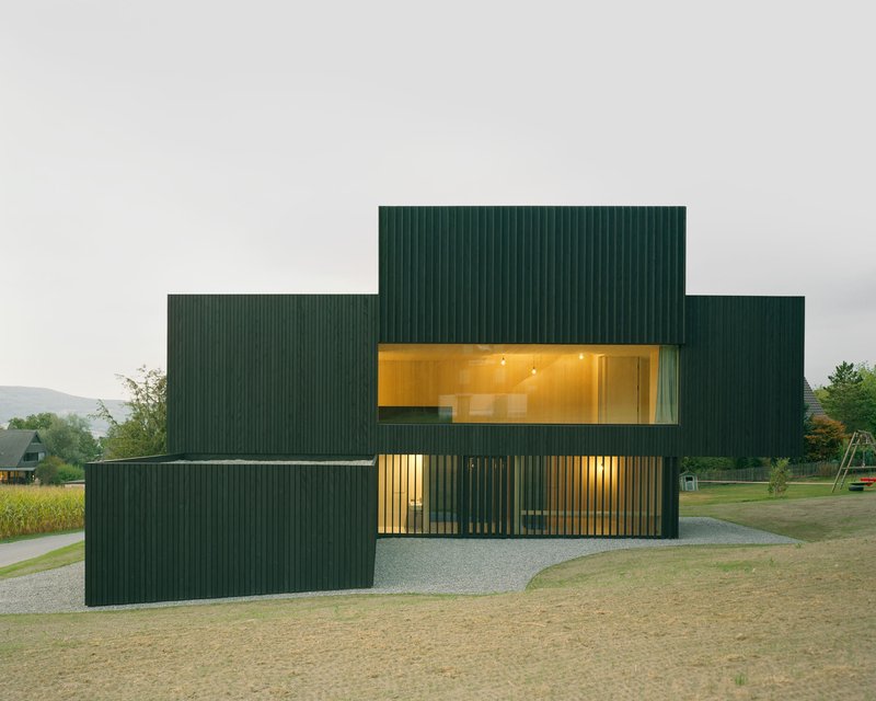 Stepped facade composition with illuminated ribbon windows at dusk in rural landscape