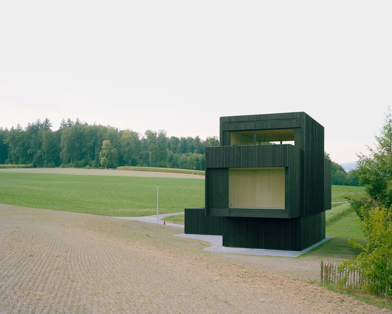 Stacked volumes clad in green corrugated siding with yellow glass openings overlooking fields and forest