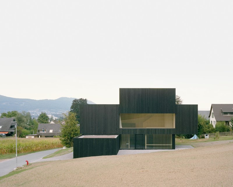 Dark ribbed timber volumes with horizontal yellow glazing set among roads and residential rooftops