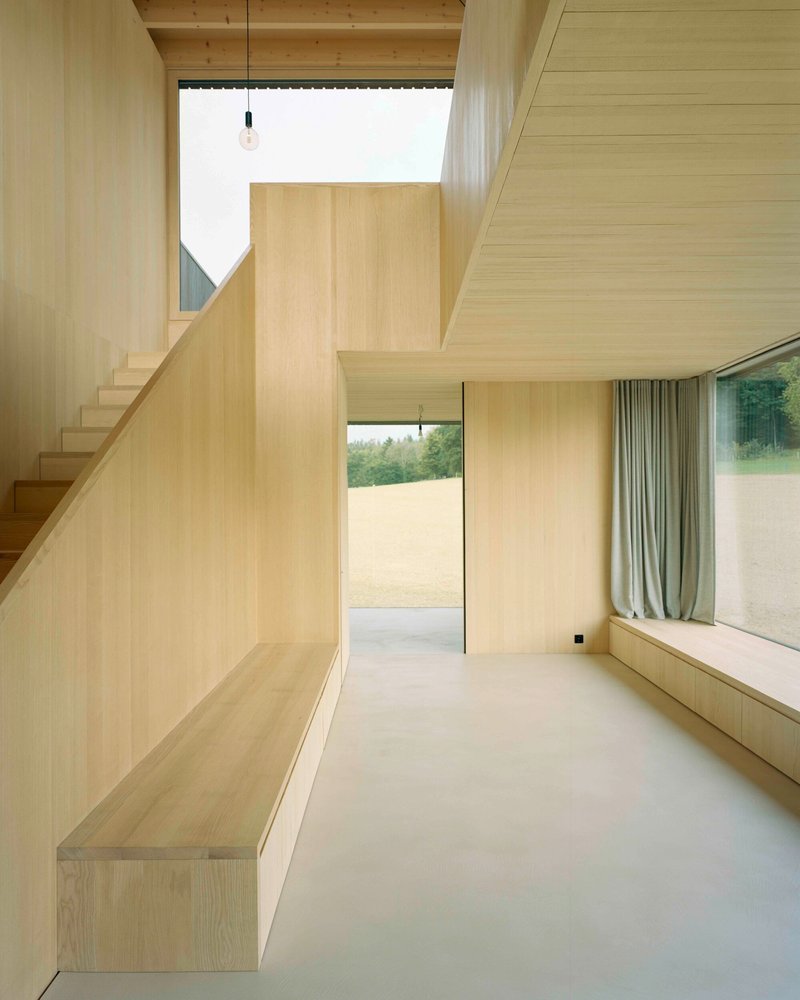 Double-height room with timber staircase and exposed beam ceiling beneath a skylight