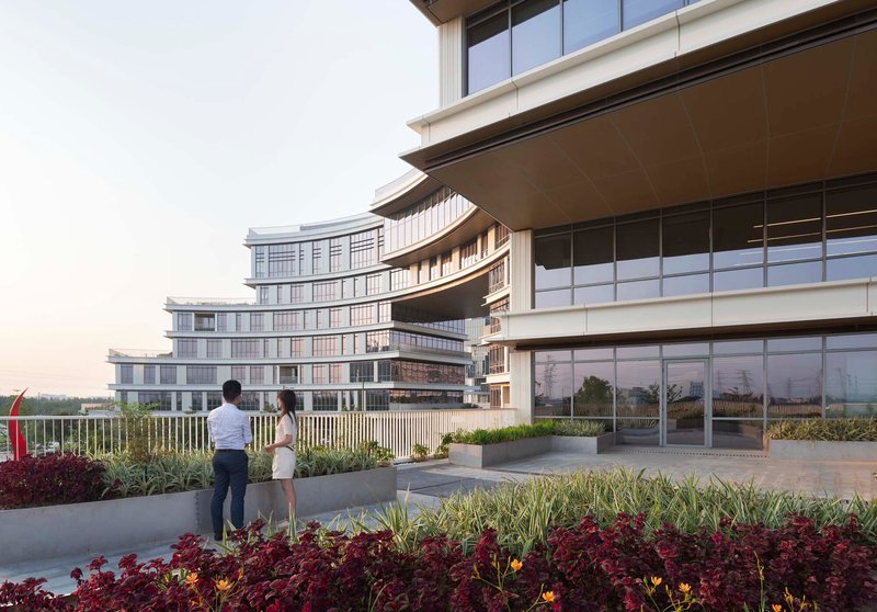 Rooftop terrace with planted beds and two people looking toward horizontal facade bands at dusk
