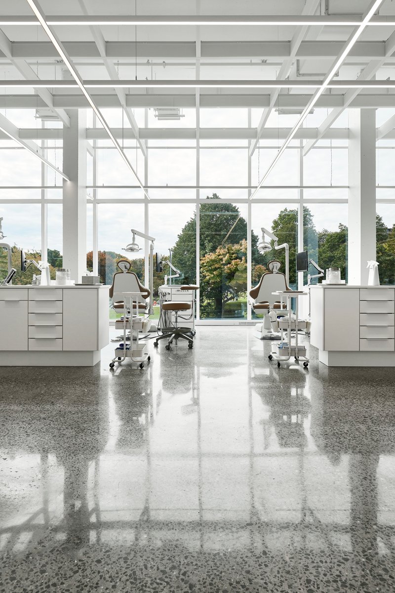 Interior workspace with dental chairs and equipment facing floor-to-ceiling windows overlooking trees
