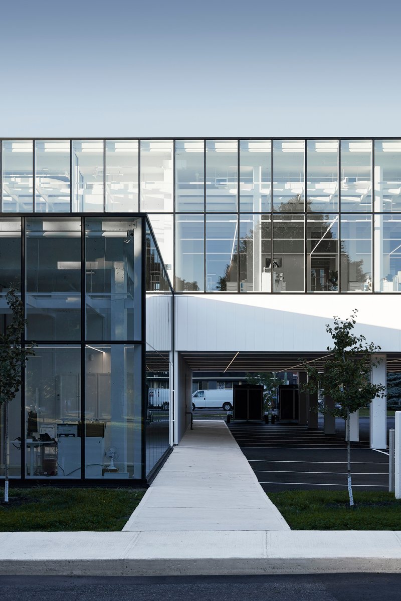 Concrete pathway leading between glass facades and a timber-clad volume at twilight