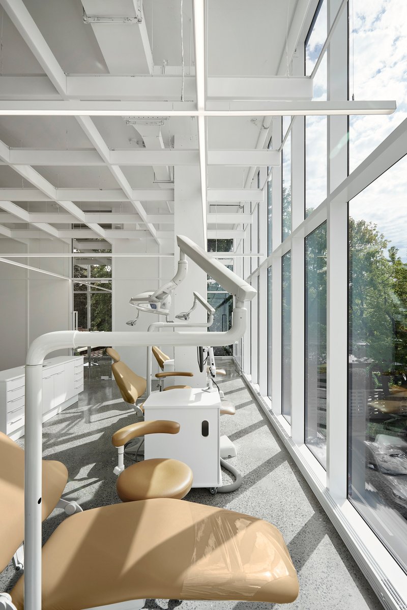 Corner workspace with dental chairs upholstered in tan vinyl beside a floor-to-ceiling glass curtain wall