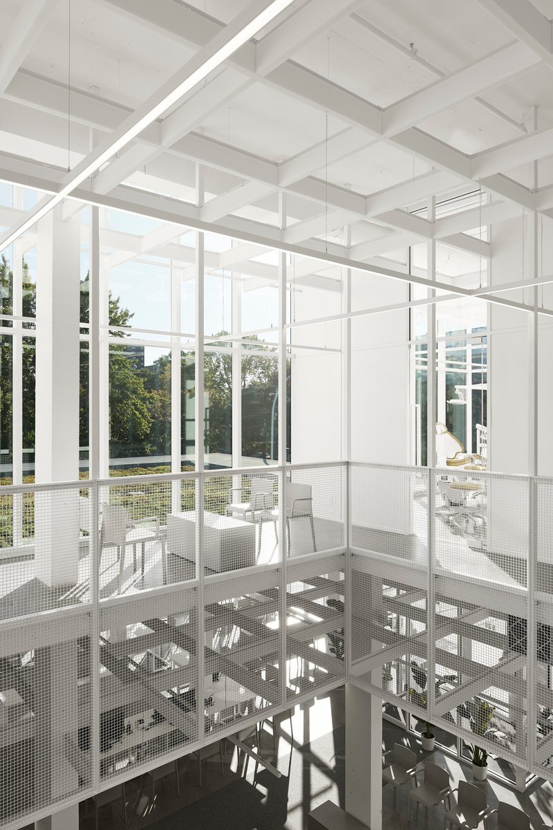 White steel framework and perforated metal mezzanine floor with double-height glazed walls overlooking garden