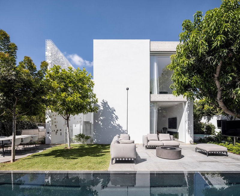 Pool terrace with white furniture and lawn beneath two-story glazed volume and pixelated screen