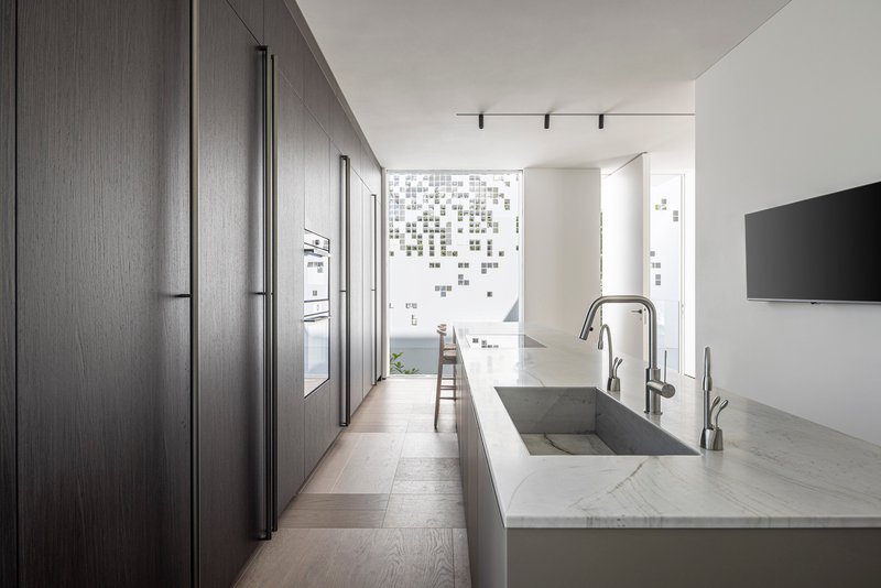Galley kitchen with dark wood cabinetry and marble waterfall island facing perforated facade screen