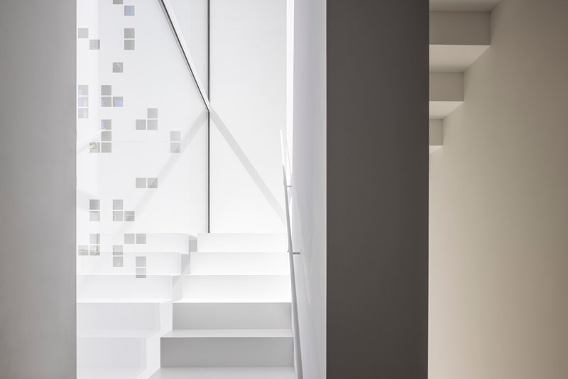 White floating staircase with metal handrail beside a wall with scattered square grey tiles