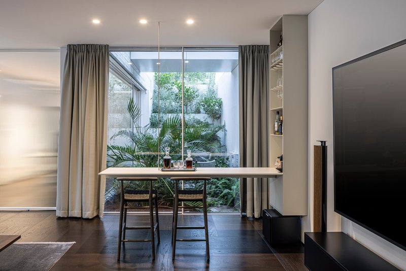 Dining area with two chairs facing a glazed courtyard filled with potted palms and greenery
