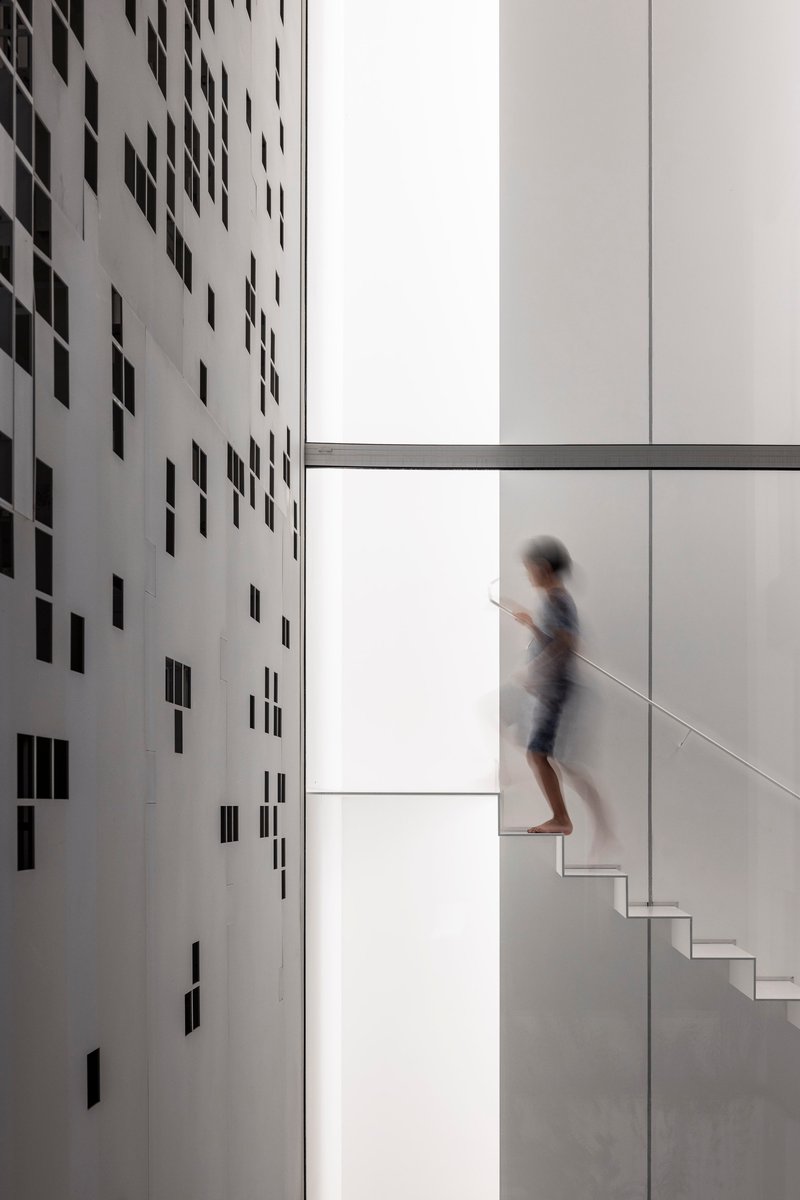 Person ascending a white staircase beside a perforated wall casting scattered shadows in bright daylight