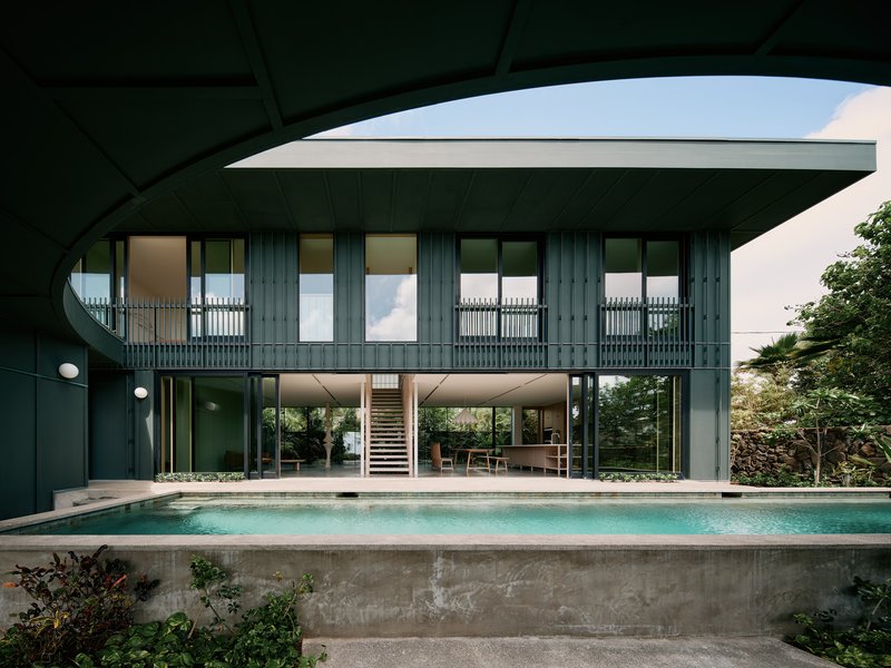 Rear facade with dark vertical cladding and open ground floor overlooking the elevated concrete lap pool